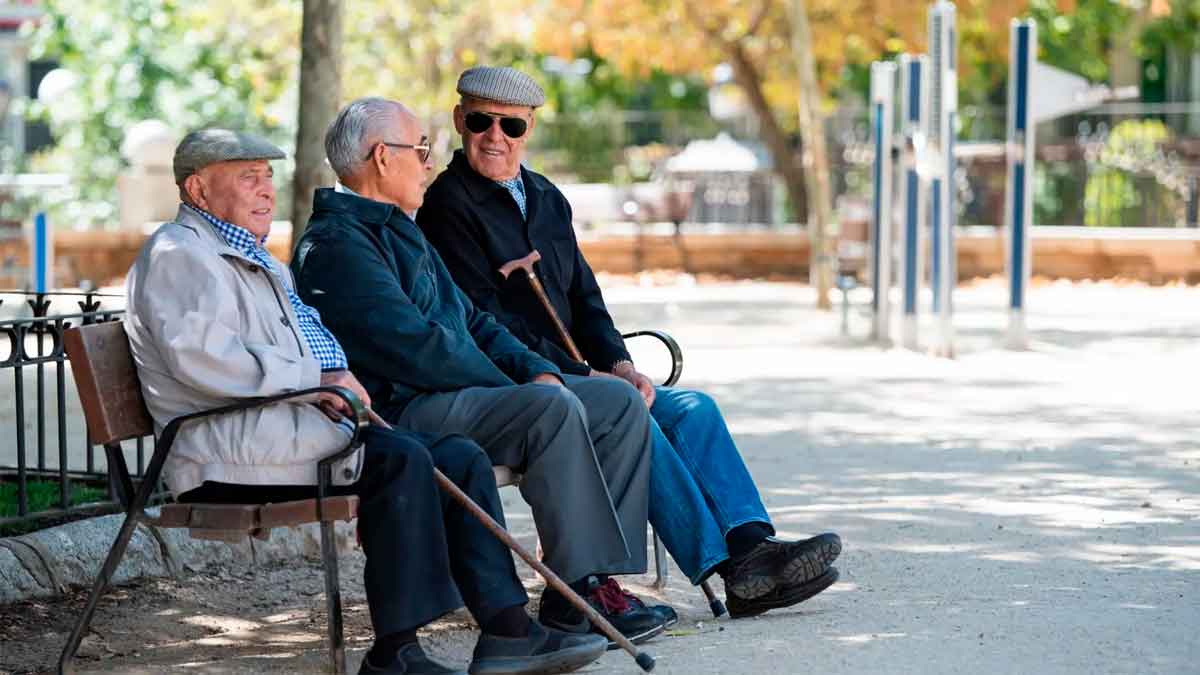 Tres jubilados conversan sentados en un banco de un parque tras la subida de pensiones que eleva el IRPF en 2025