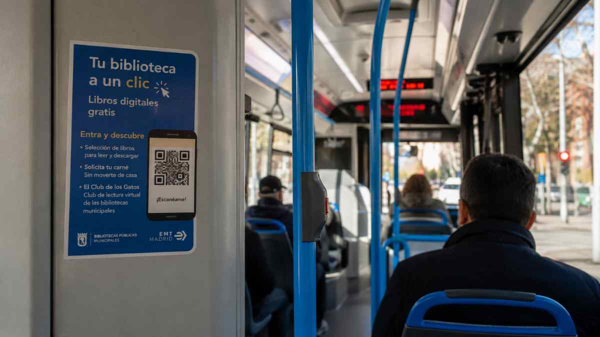 Usuarios viajan en un autobús de EMT Madrid junto al cartel de “Tu biblioteca a un clic” para acceder gratis a libros digitales mediante código QR