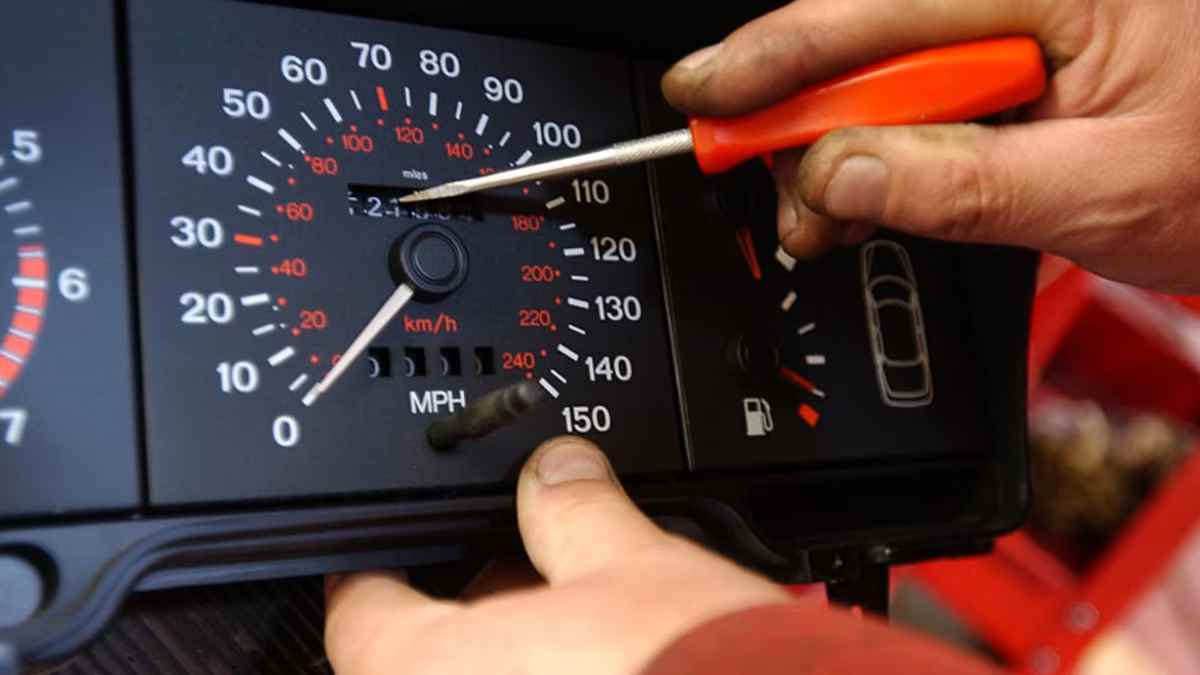 Manos manipulando cuentakilómetros de coche con destornillador, posible delito de estafa.