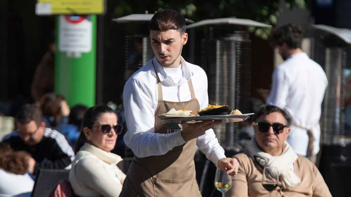 Camarero trabajando en una terraza, denuncia condiciones laborales oferta hostelería 1600 euros sin días libres.