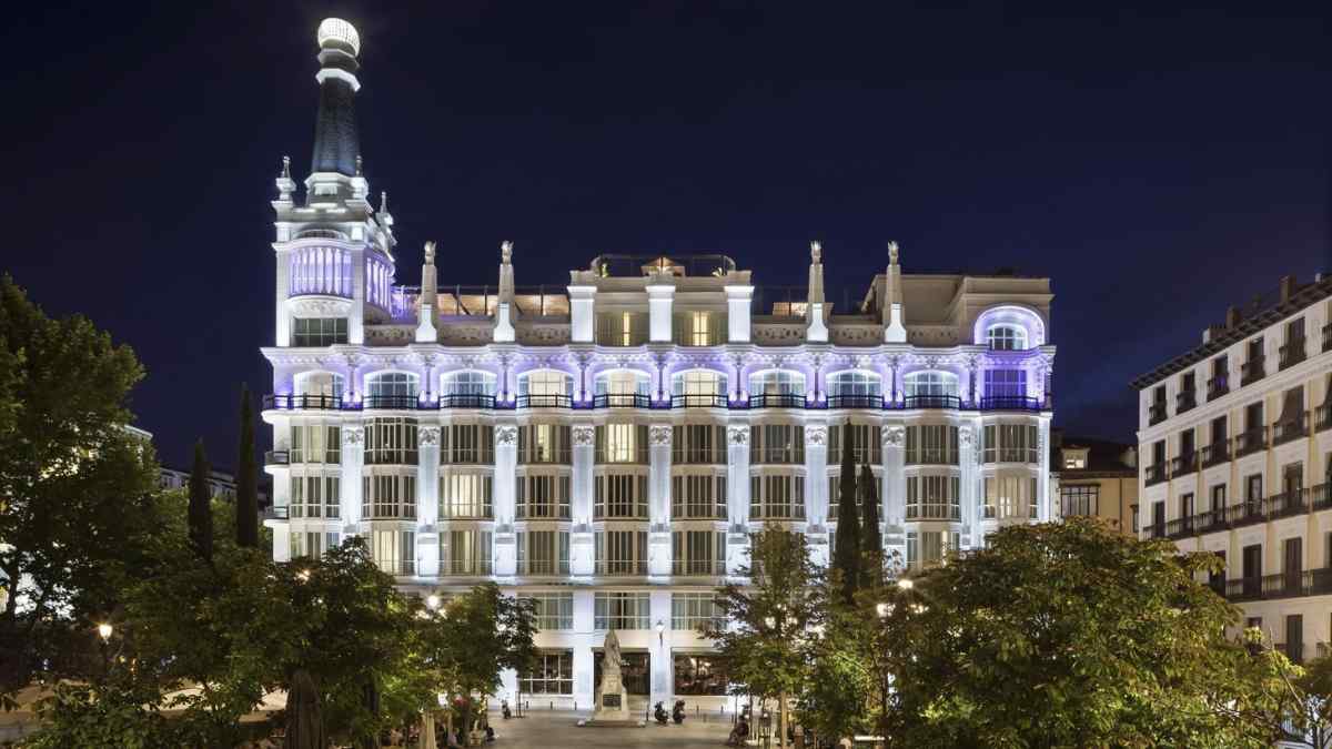 Fachada iluminada del Hotel ME Madrid Reina Victoria en la Plaza de Santa Ana durante la noche.