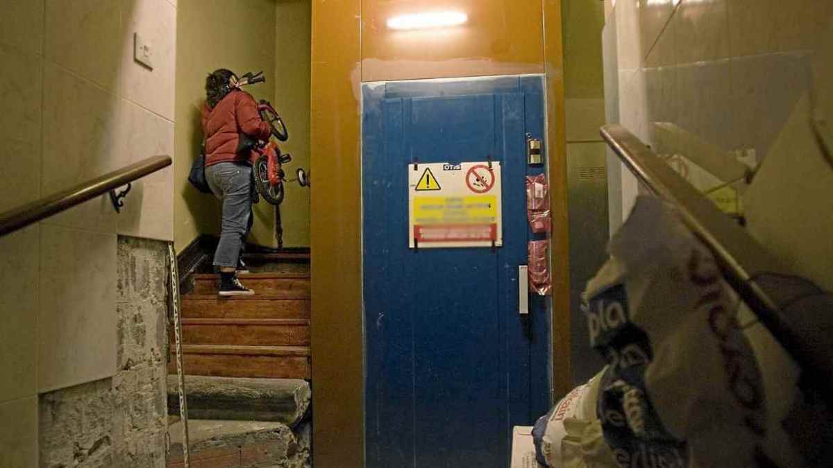 Escalera de comunidad sin accesibilidad junto a un ascensor antiguo en un edificio residencial.