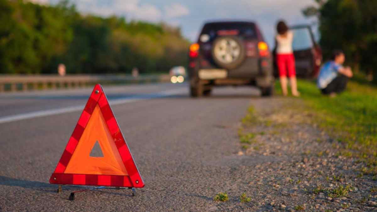 Triángulo de emergencia colocado en la carretera junto a un coche averiado.