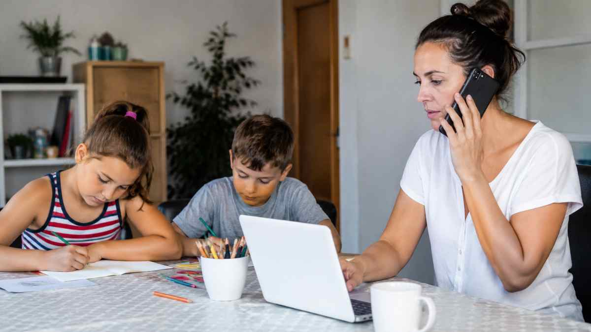 Madre teletrabajando mientras cuida de sus hijos tras el recorte de ayudas de conciliación en la Comunidad de Madrid
