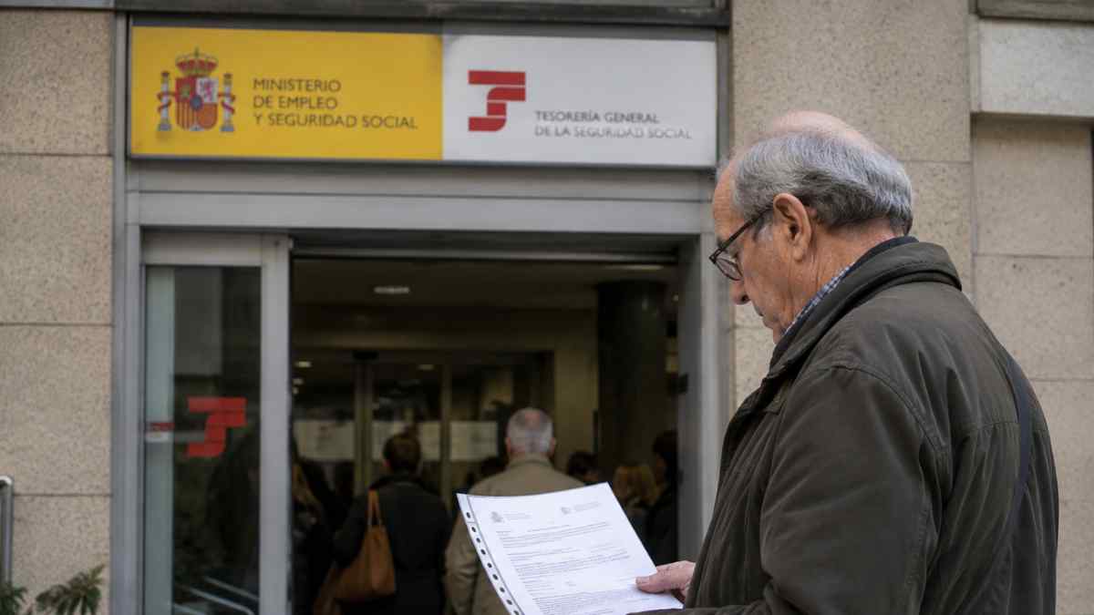 Pensionista consultando documentación frente a una oficina de la Seguridad Social para cobrar complementos a pensiones contributivas bajas