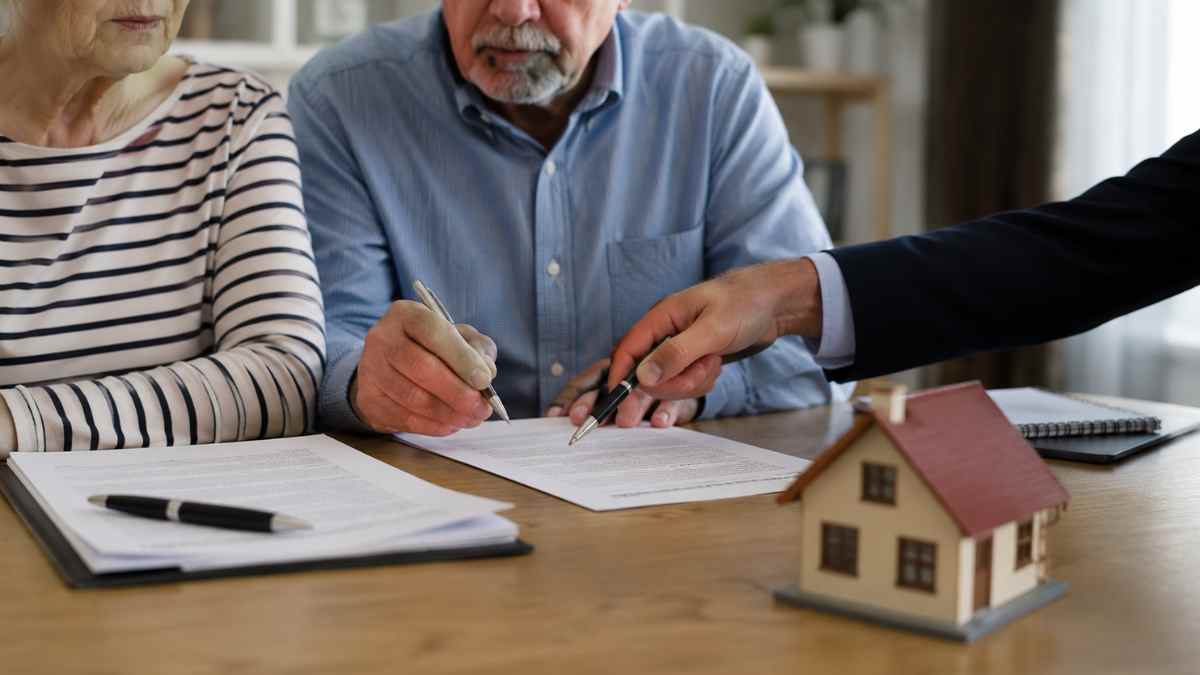 Un matrimonio mayor firma documentos relacionados con una vivienda junto a un asesor durante un proceso de herencia familiar.
