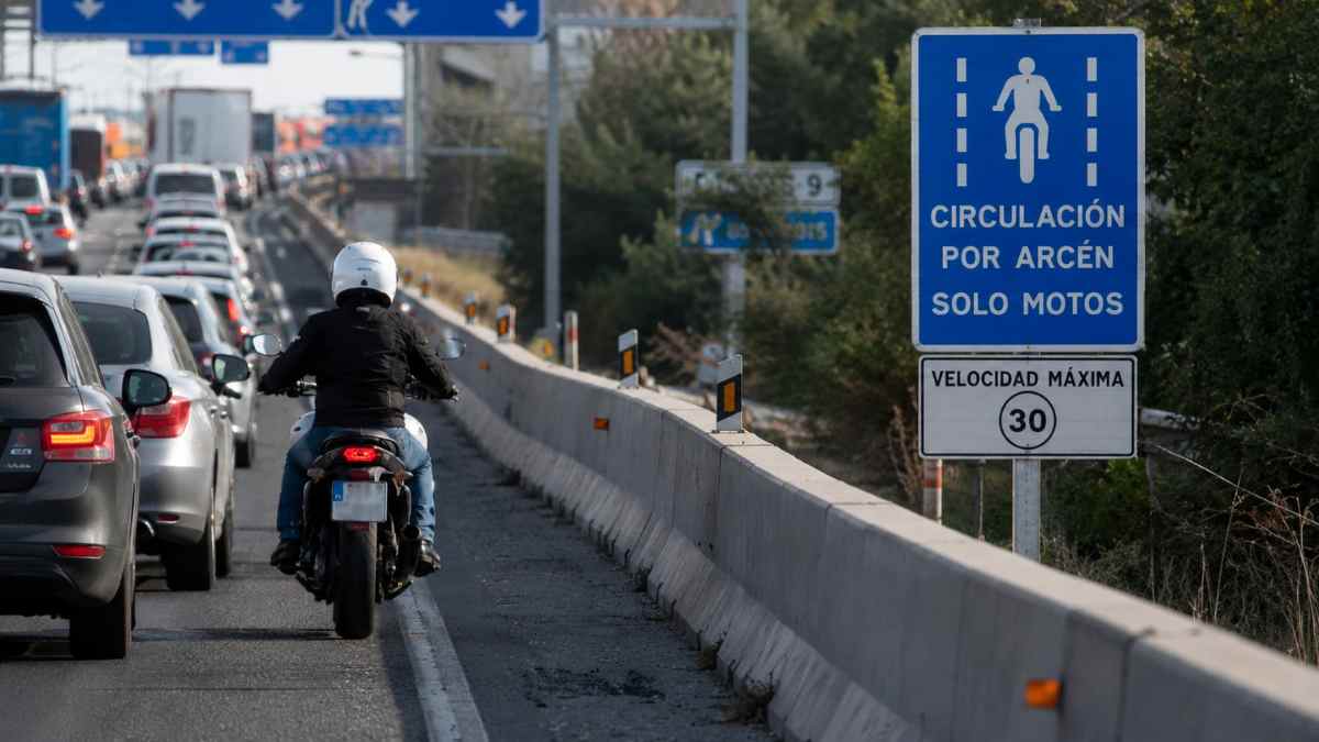 Una motocicleta circula por el arcén derecho en un atasco tras la nueva normativa de la DGT que permite hacerlo a 30 km/h.