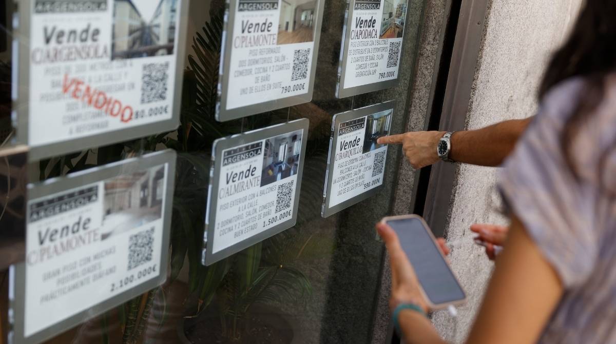 Personas consultando anuncios de viviendas en el escaparate de una inmobiliaria en Madrid ante la subida de los precios.