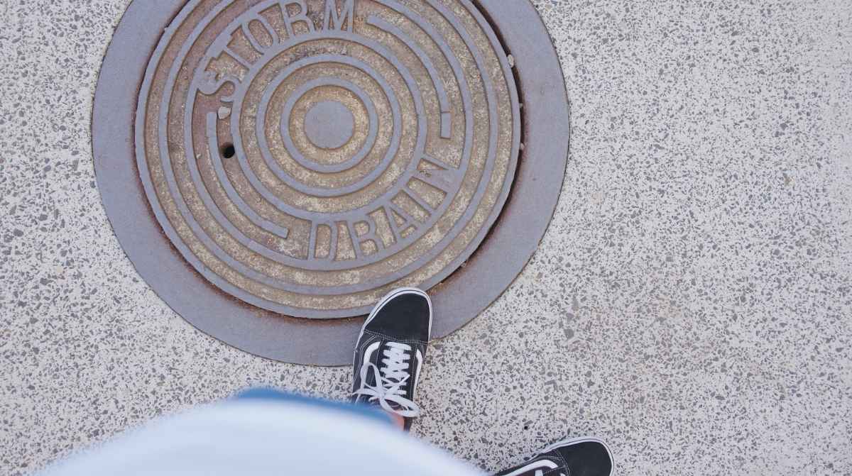 Tapa de alcantarilla redonda en una acera junto a los pies de una persona