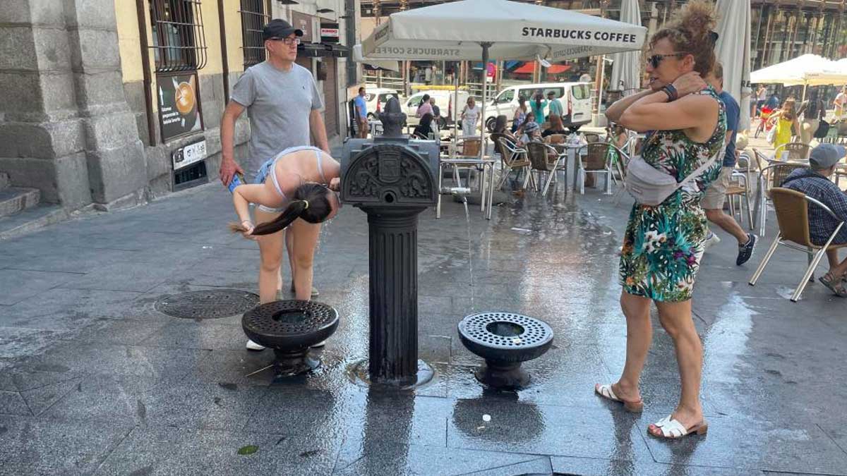 Personas refrescándose en una fuente pública durante aviso naranja por calor en Madrid