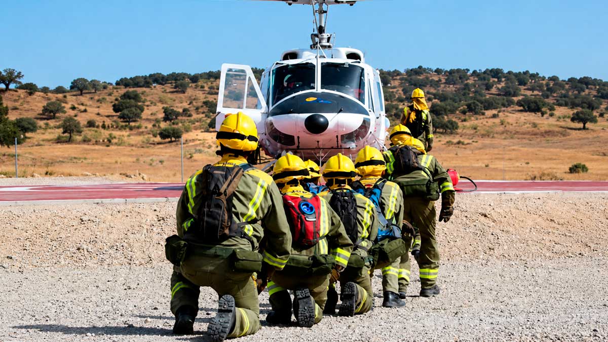 Bomberos forestales de Madrid preparados ante un helicóptero en zona rural