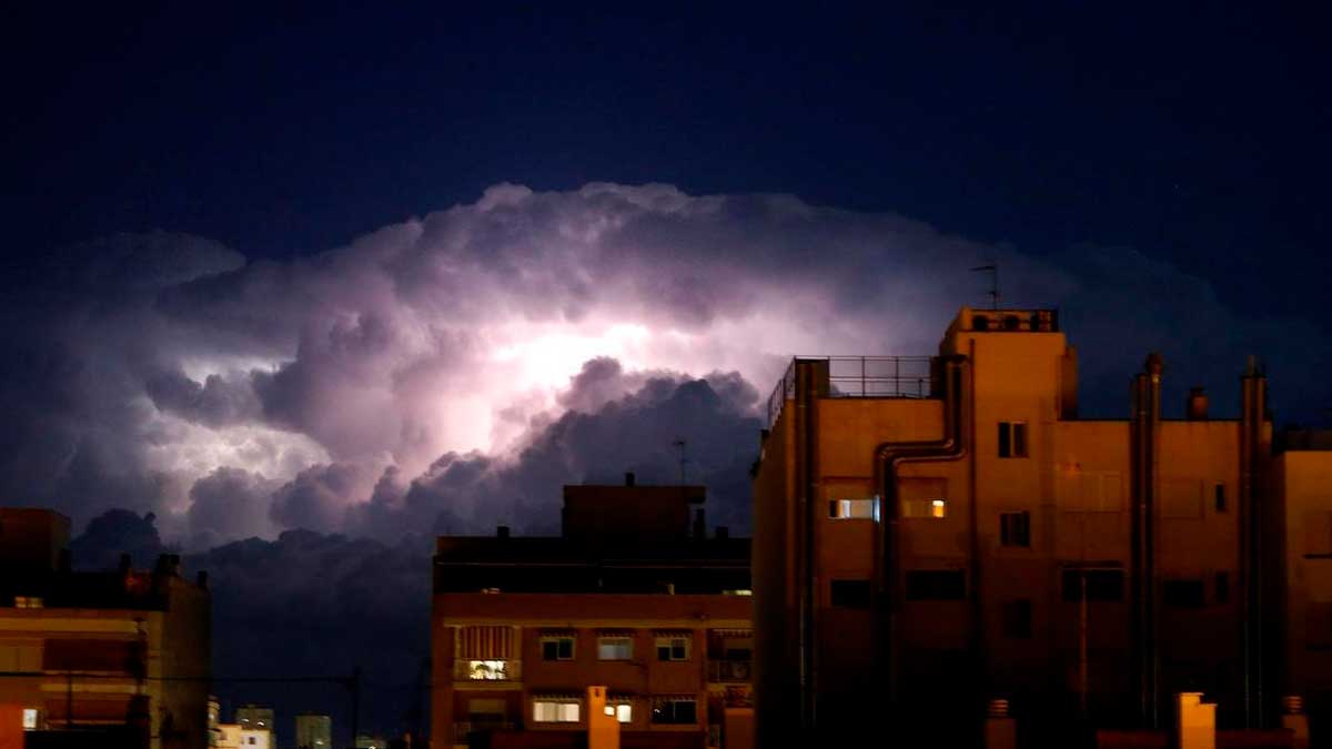 Nube de tormenta iluminada por rayos sobre edificios en Madrid durante riesgo extremo de incendios