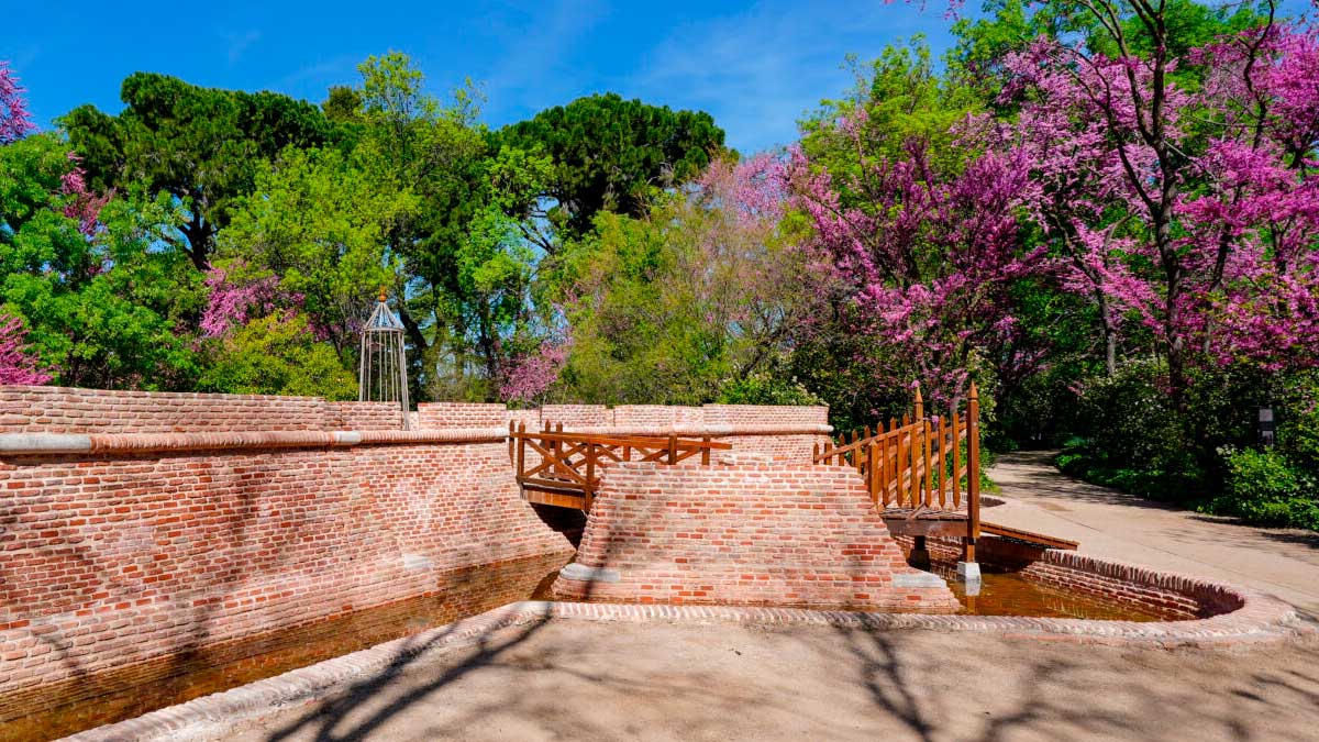 Puente de ladrillo en parque histórico de Madrid rodeado de árboles y flores primaverales