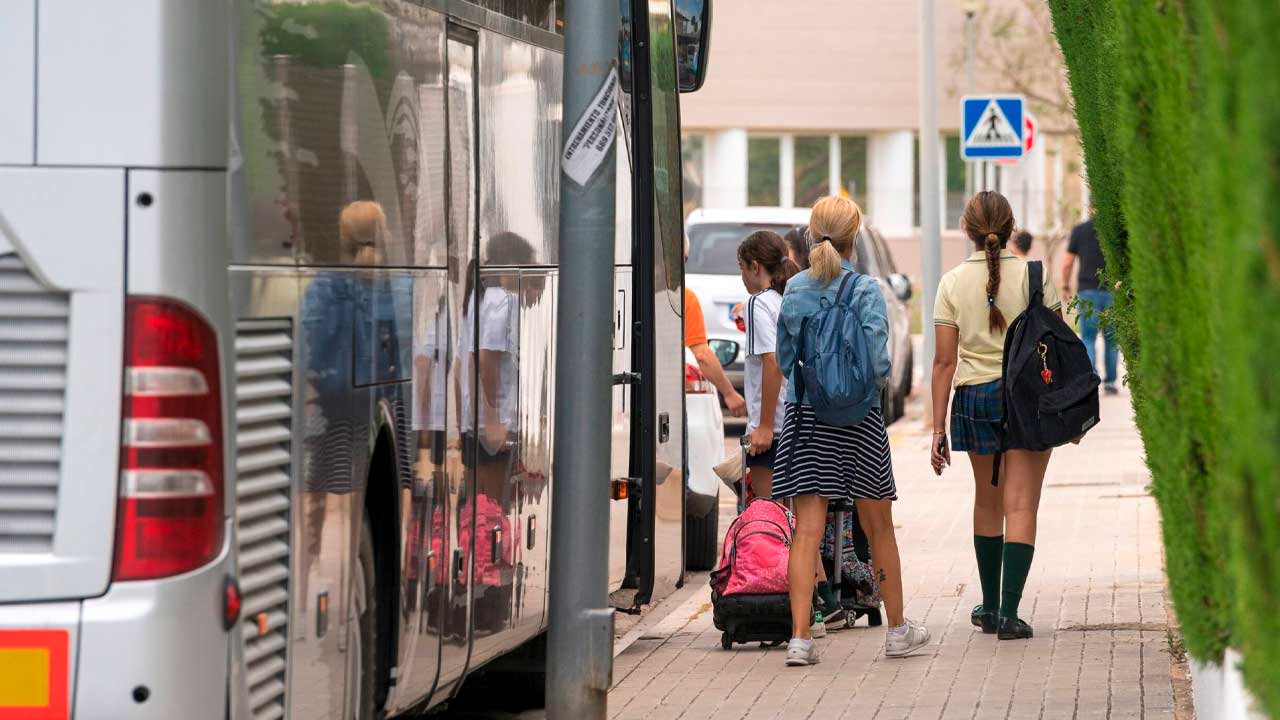 Estudiantes junto a un autobús de transporte escolar