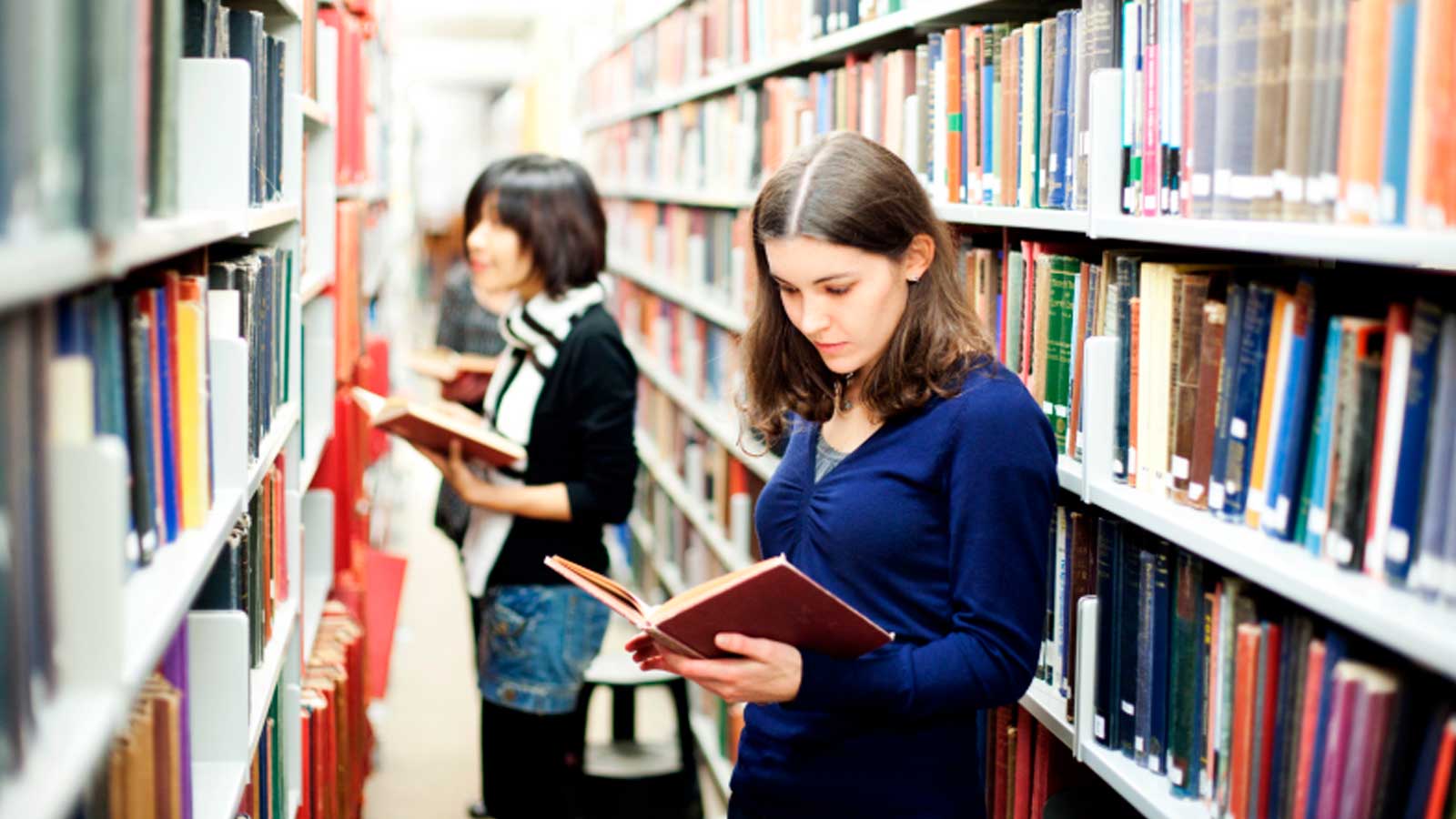 Jóvenes consultando libros en una biblioteca, uno de los servicios municipales que abren este sábado en Madrid