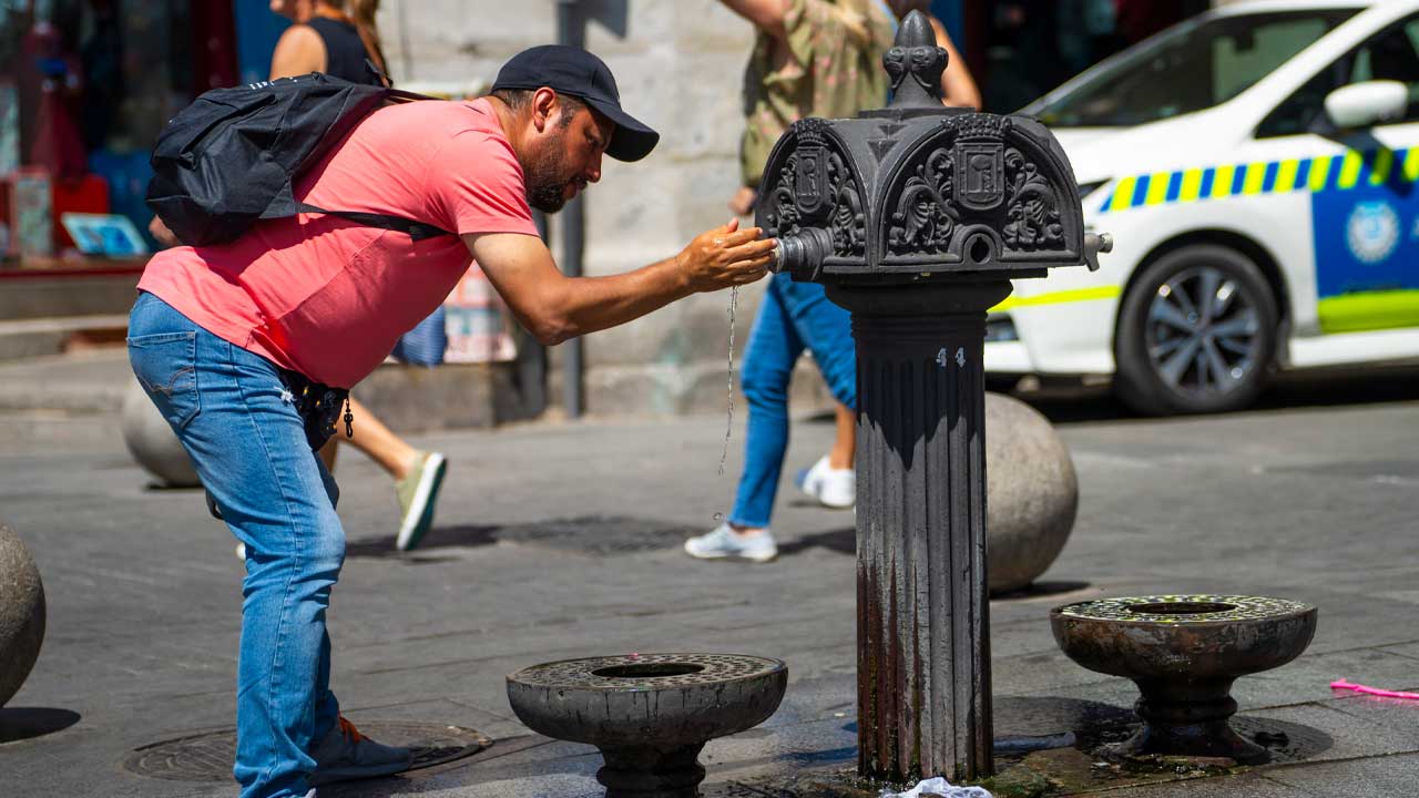 Un hombre bebe agua de una fuente durante una jornada de calor en Madrid