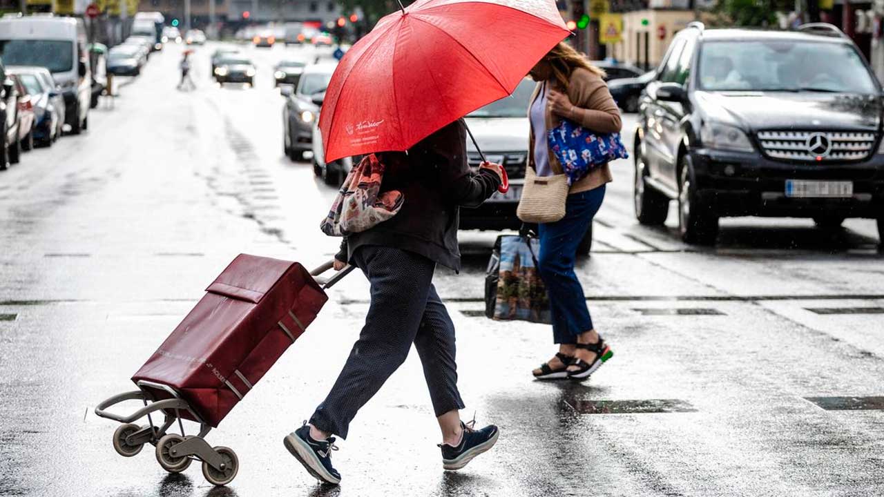 Dos mujeres con paraguas cruzan una calle de Madrid durante una jornada de lluvia