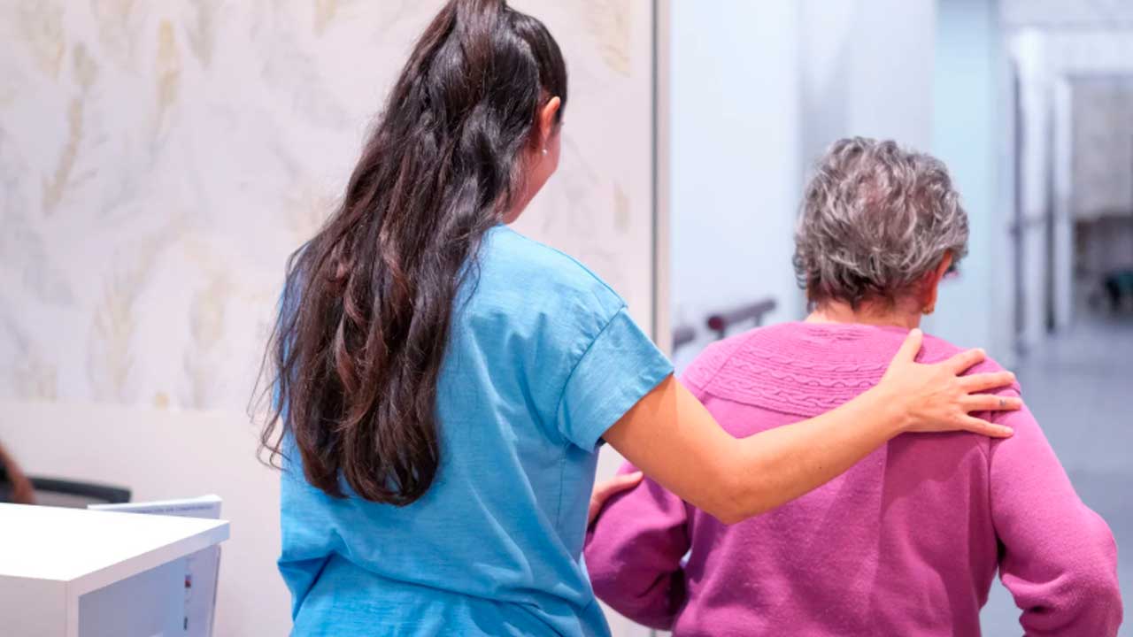 Cuidadora acompaña a una mujer mayor dependiente en una residencia