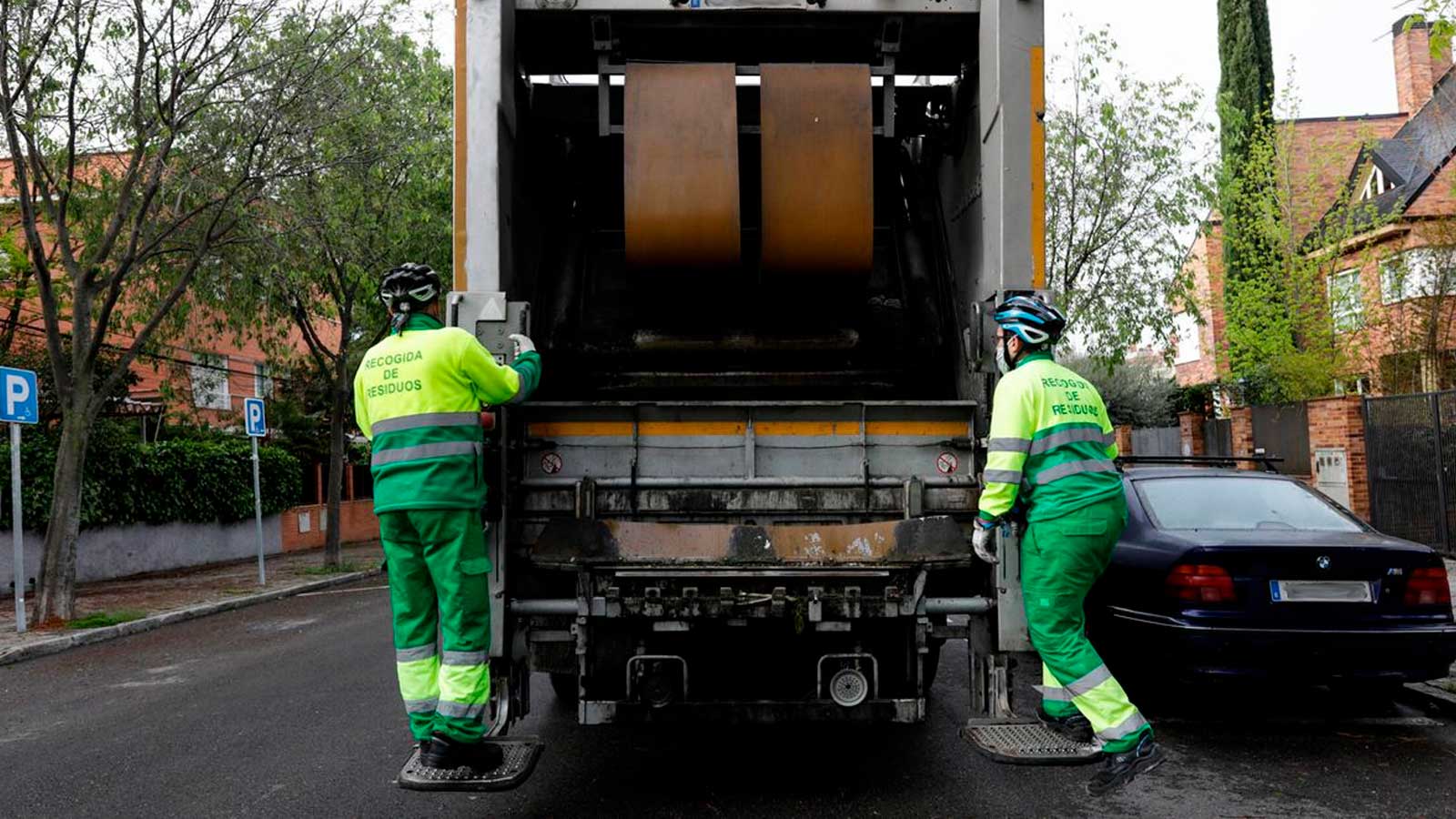 Trabajadores del servicio de recogida de residuos junto a un camión de basura en Madrid