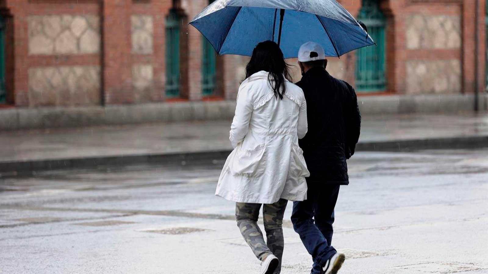 Dos personas caminan bajo un paraguas mientras llueve en una calle de Madrid.