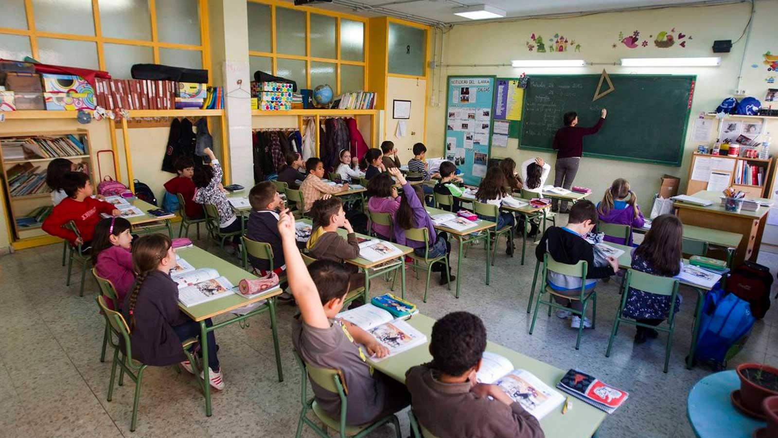 Alumnos de un colegio de Madrid levantan la mano durante una clase con su profesora.