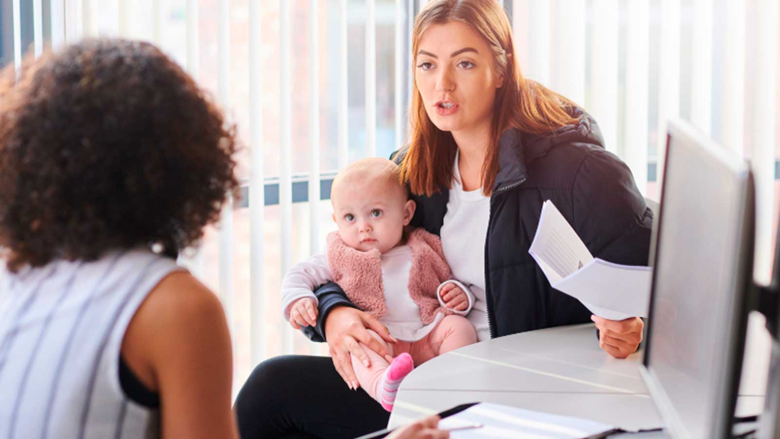 Madre con su bebé durante una consulta con una trabajadora social para recibir orientación sobre ayudas familiares.