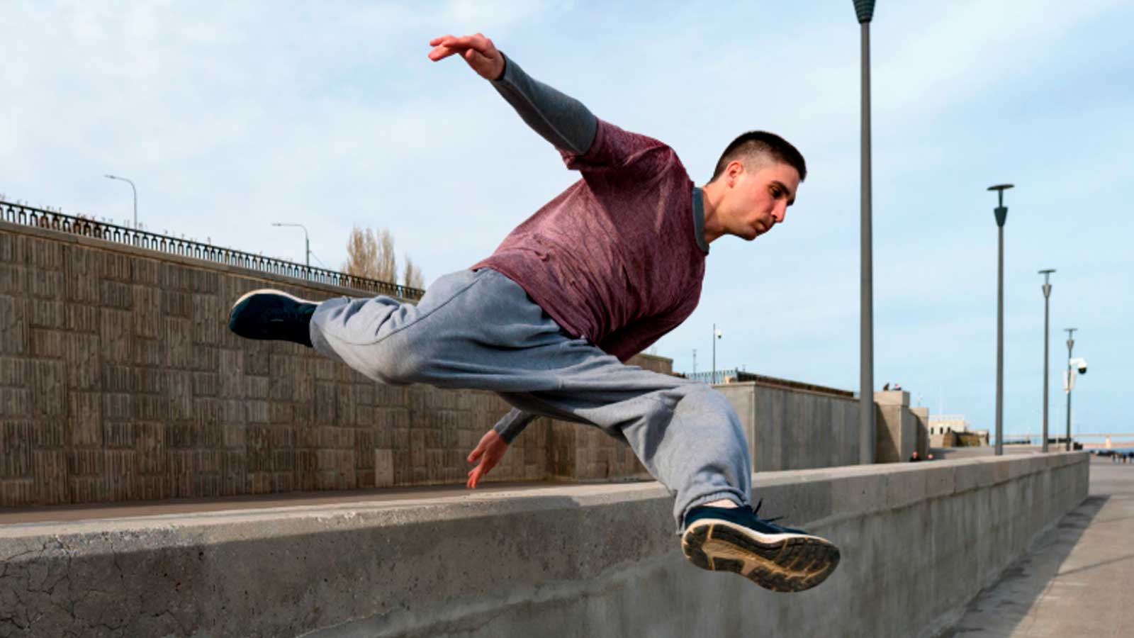 Joven practicando parkour y saltando un muro de hormigón durante un ejercicio al aire libre