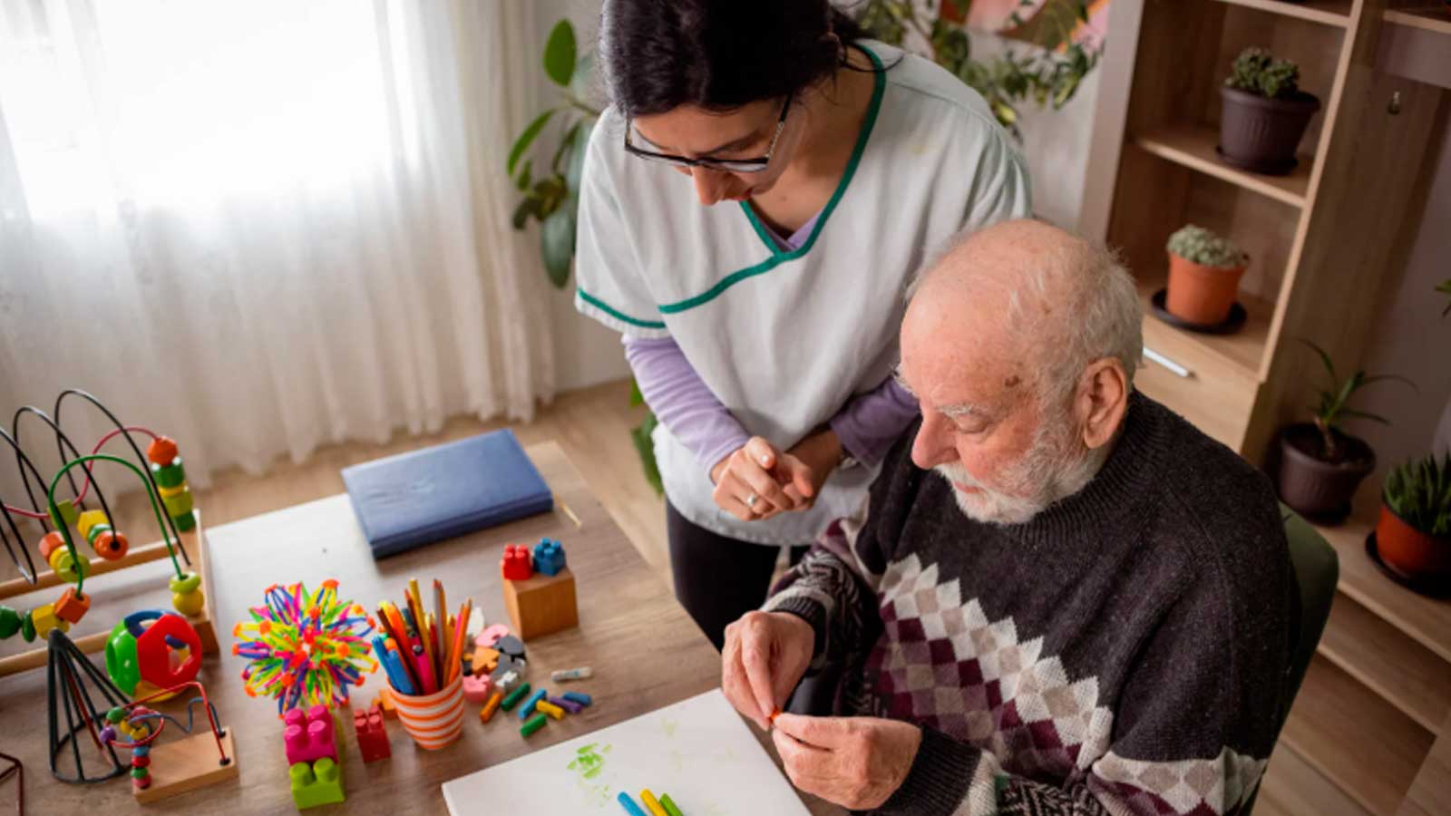 Una cuidadora acompaña a un hombre mayor durante una actividad de estimulación cognitiva con materiales de colores.