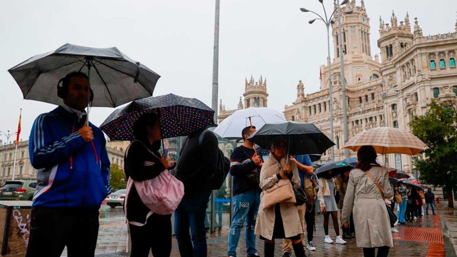 Peatones con paraguas bajo la lluvia frente al Palacio de Cibeles en Madrid