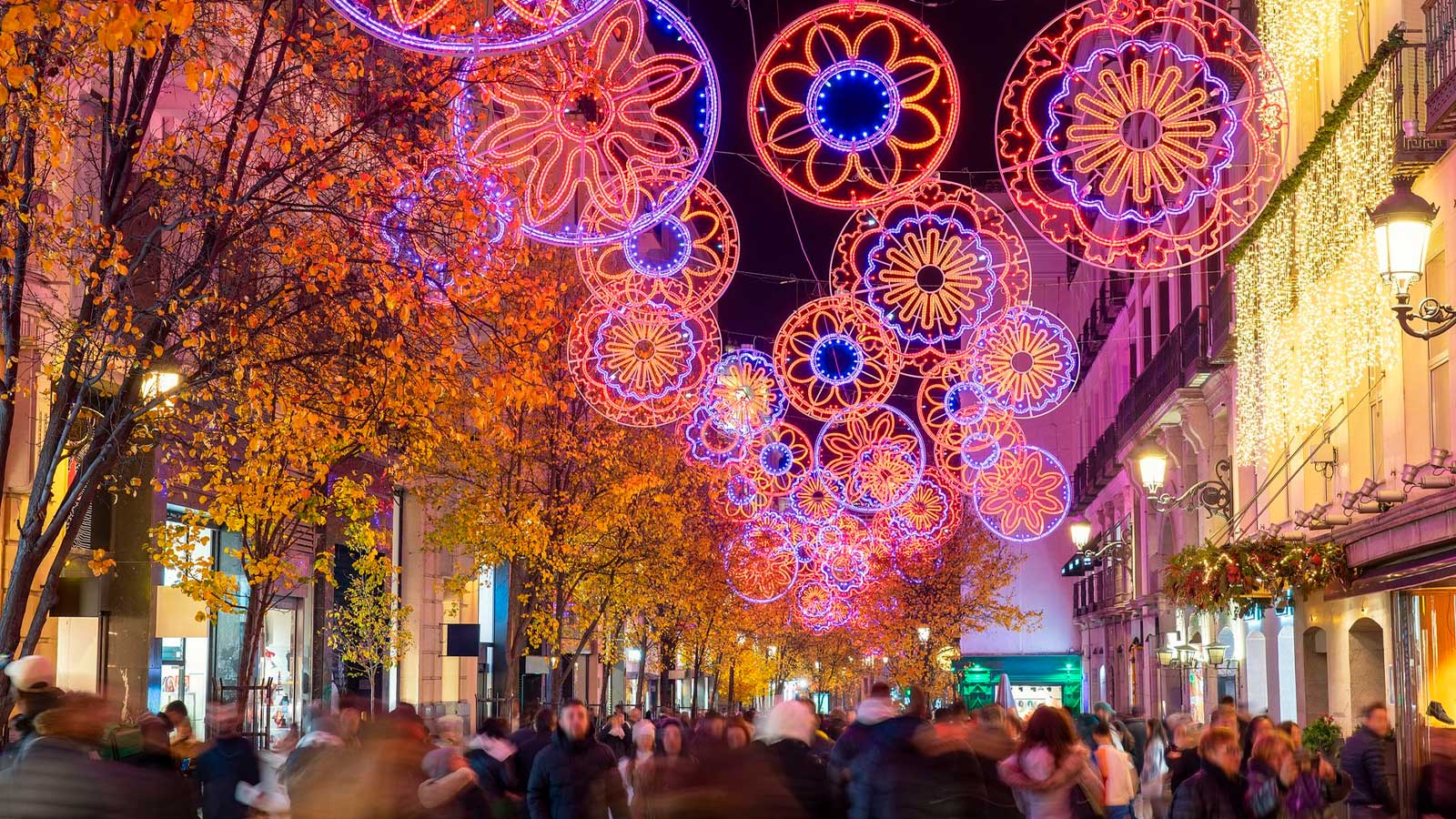 Calle de Madrid decorada con luces de Navidad de colores y numerosas personas paseando