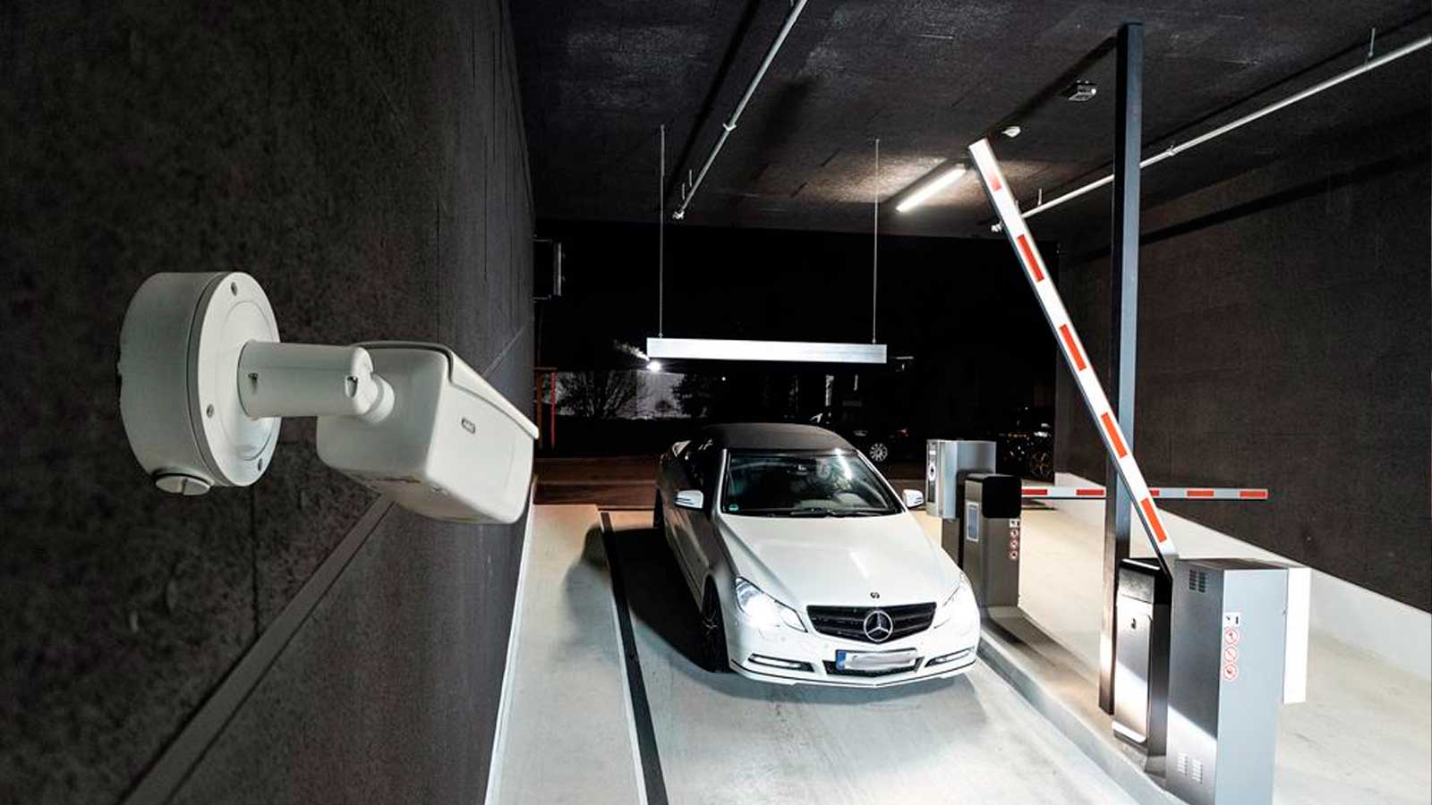 Cámara de reconocimiento de matrículas junto a un coche y una barrera de acceso a un aparcamiento subterráneo.
