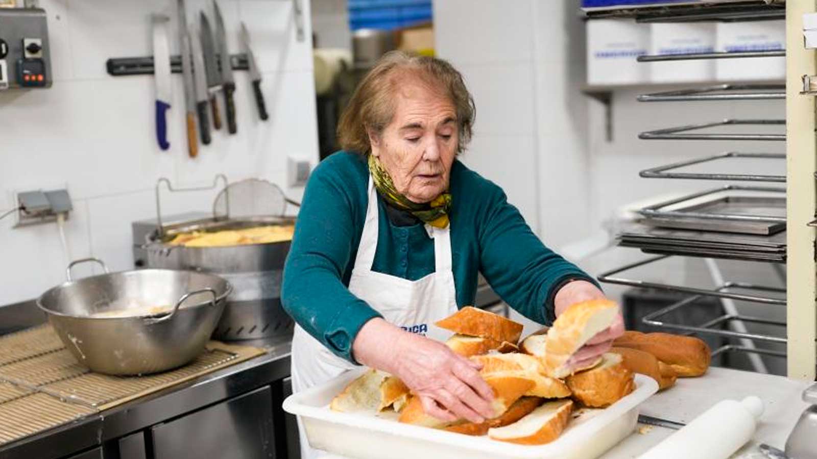 Mujer mayor preparando pan en una cocina, una actividad relacionada con la vida cotidiana y el envejecimiento activo.