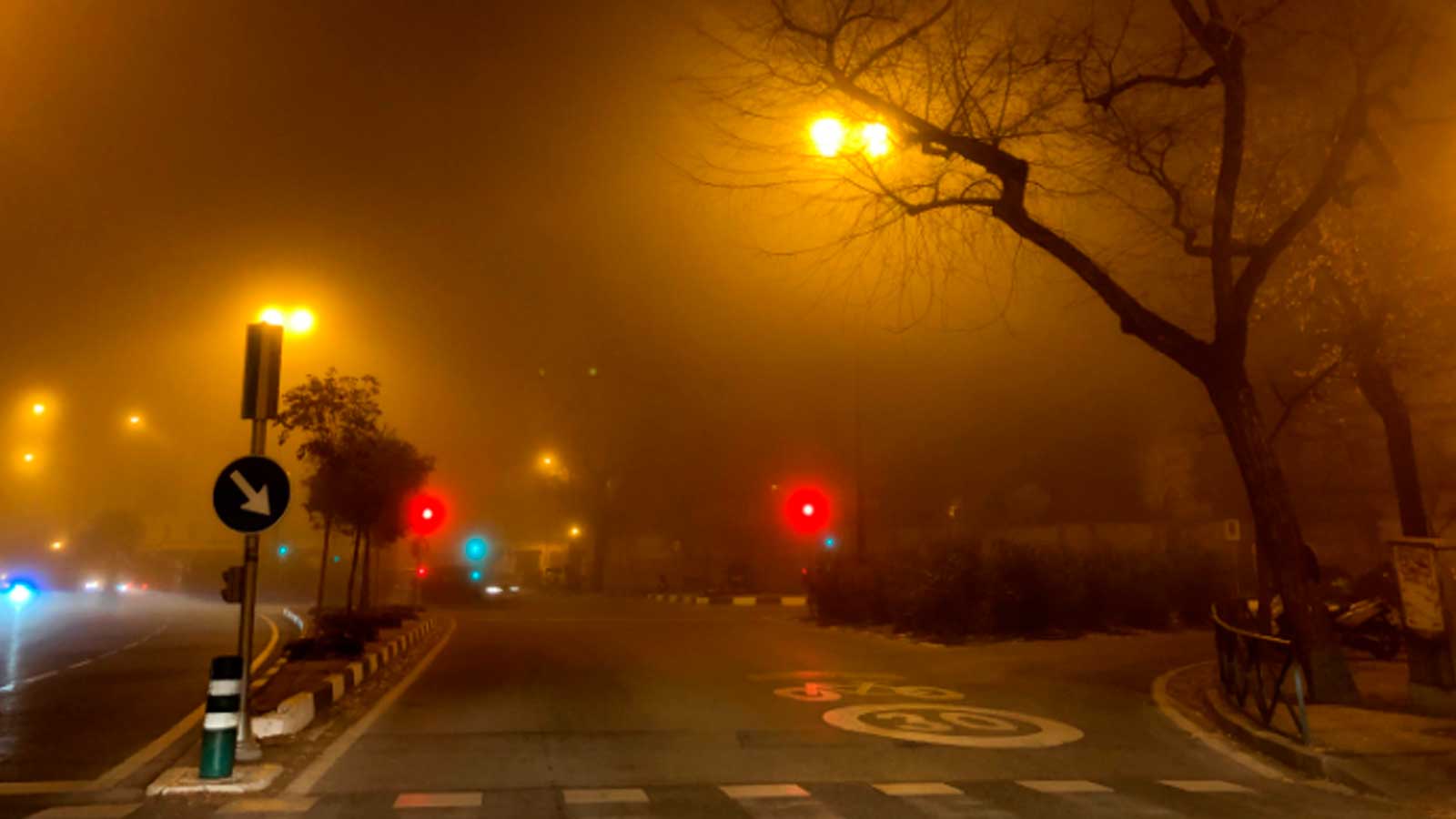 Niebla densa reduce la visibilidad en una carretera iluminada por farolas y semáforos.