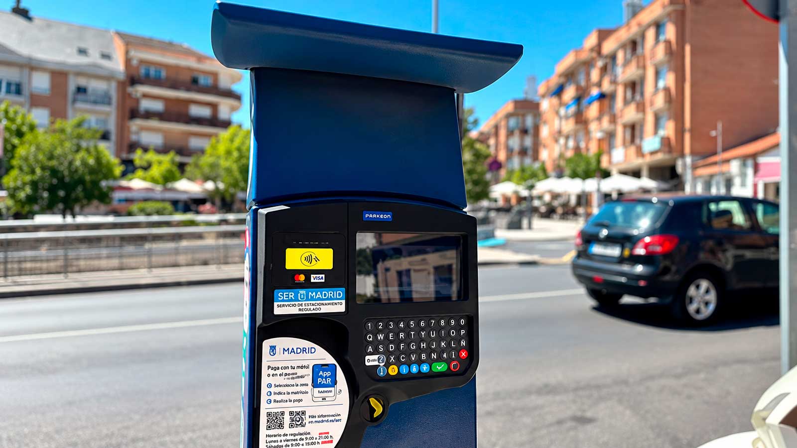 Parquímetro del SER de Madrid junto a una calle con coches estacionados.