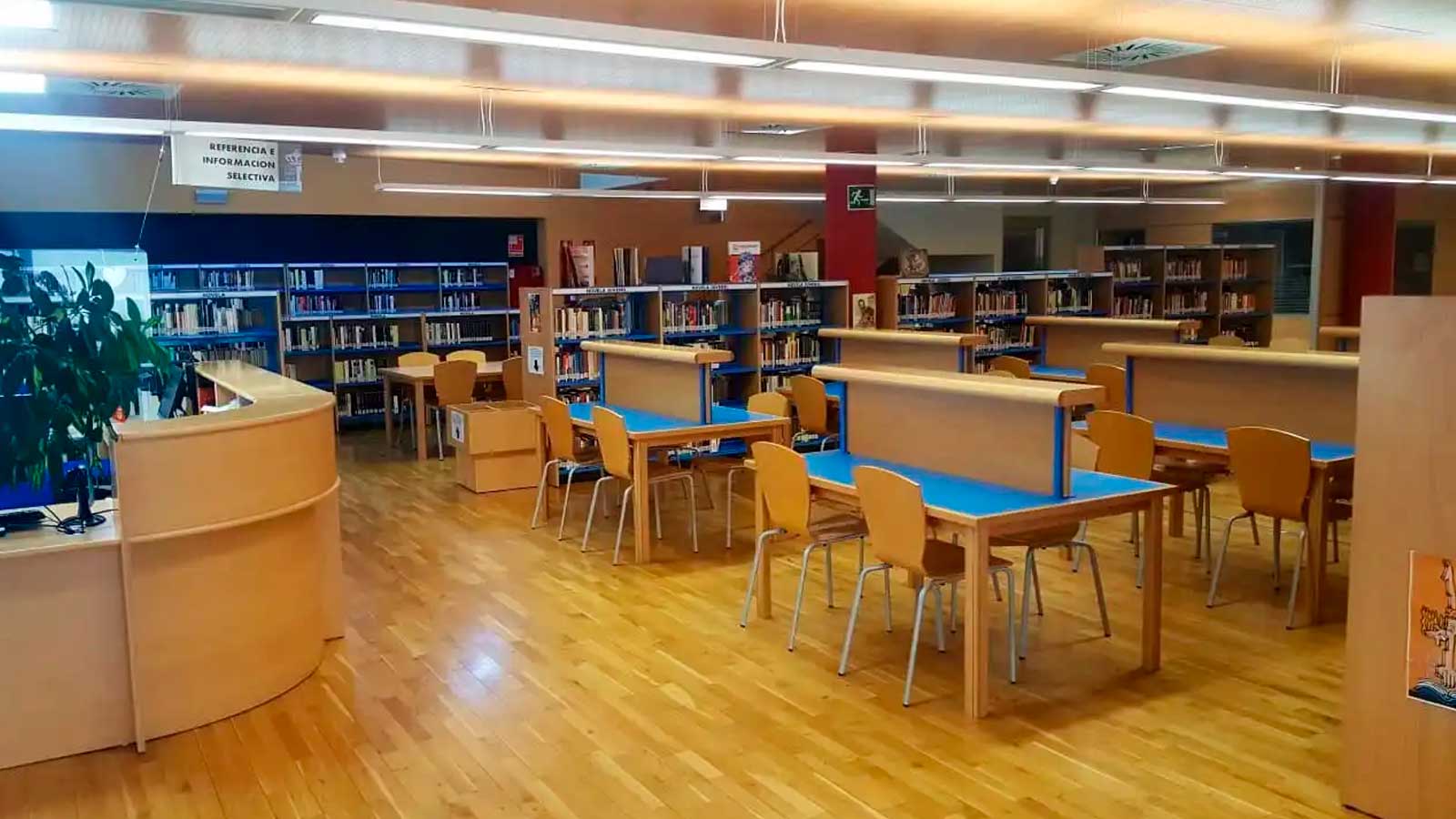 Interior de una biblioteca con mesas de estudio y estanterías de libros, para ilustrar las oposiciones de auxiliar de biblioteca en Arroyomolinos.