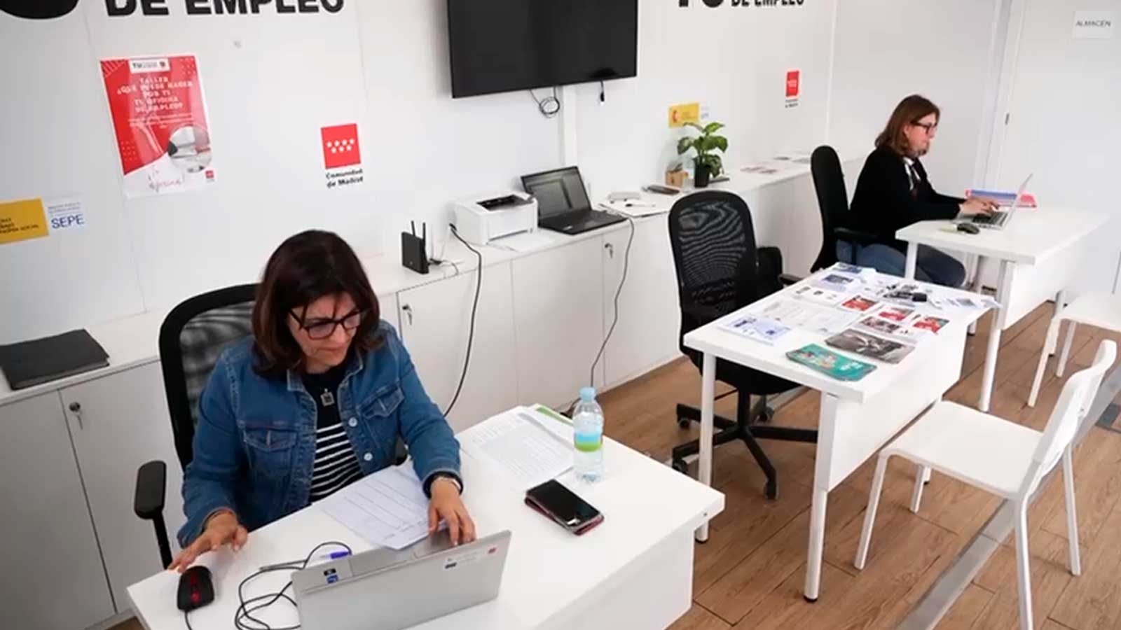 Interior de una oficina de empleo de la Comunidad de Madrid con trabajadoras utilizando ordenadores.
