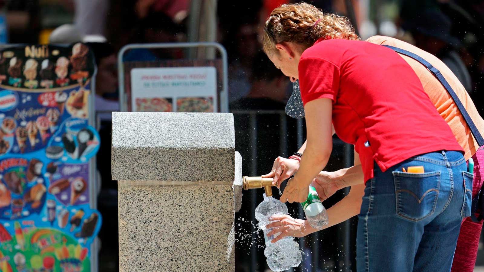 Personas rellenando botellas en una fuente de agua potable de Madrid