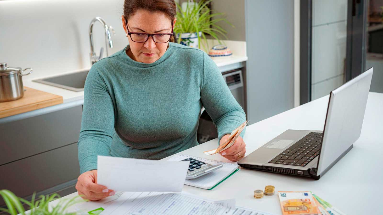 Mujer revisando facturas y gastos del hogar con una calculadora y un ordenador portátil.