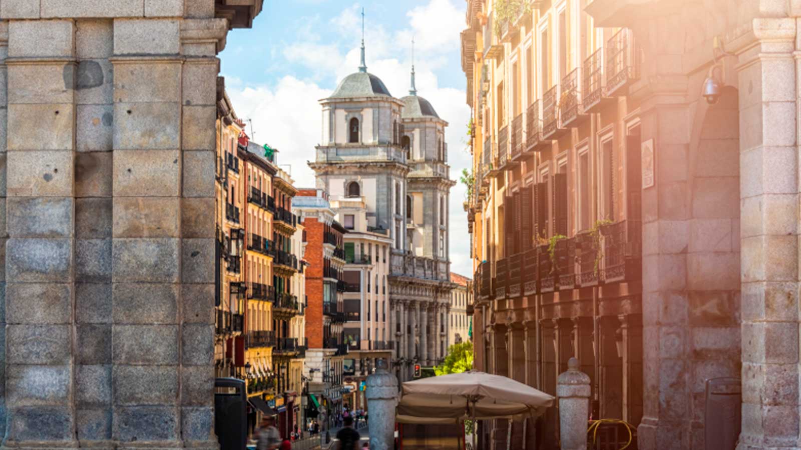 Vista de una calle del centro de Madrid con la iglesia de San Isidro al fondo y el sol iluminando los edificios