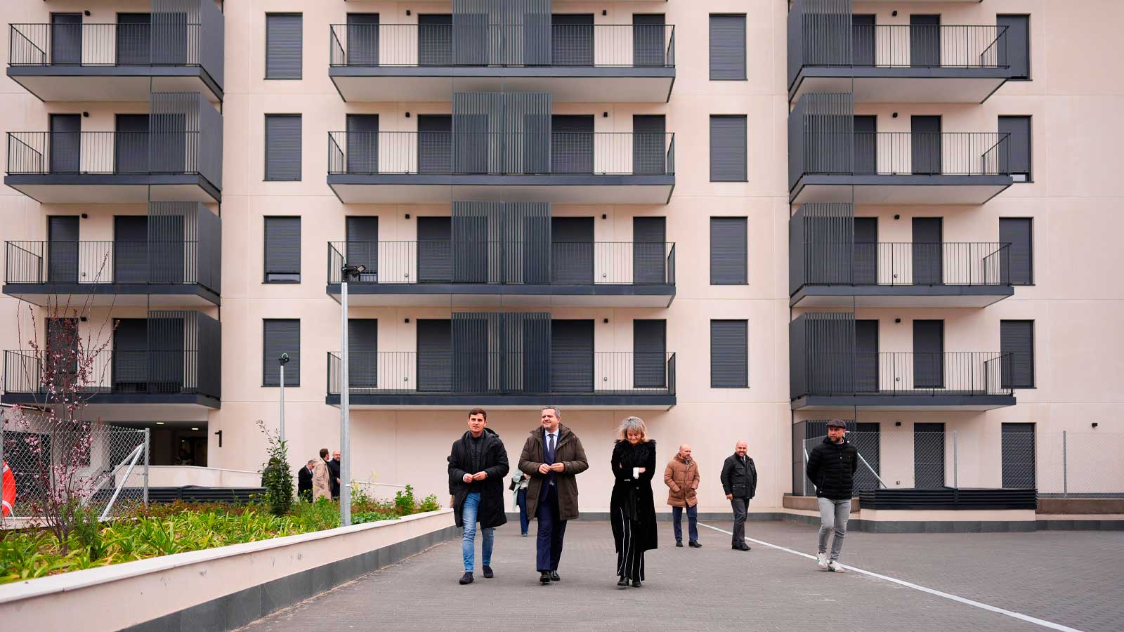 Edificio de viviendas públicas en la Comunidad de Madrid con varias personas frente a su fachada.